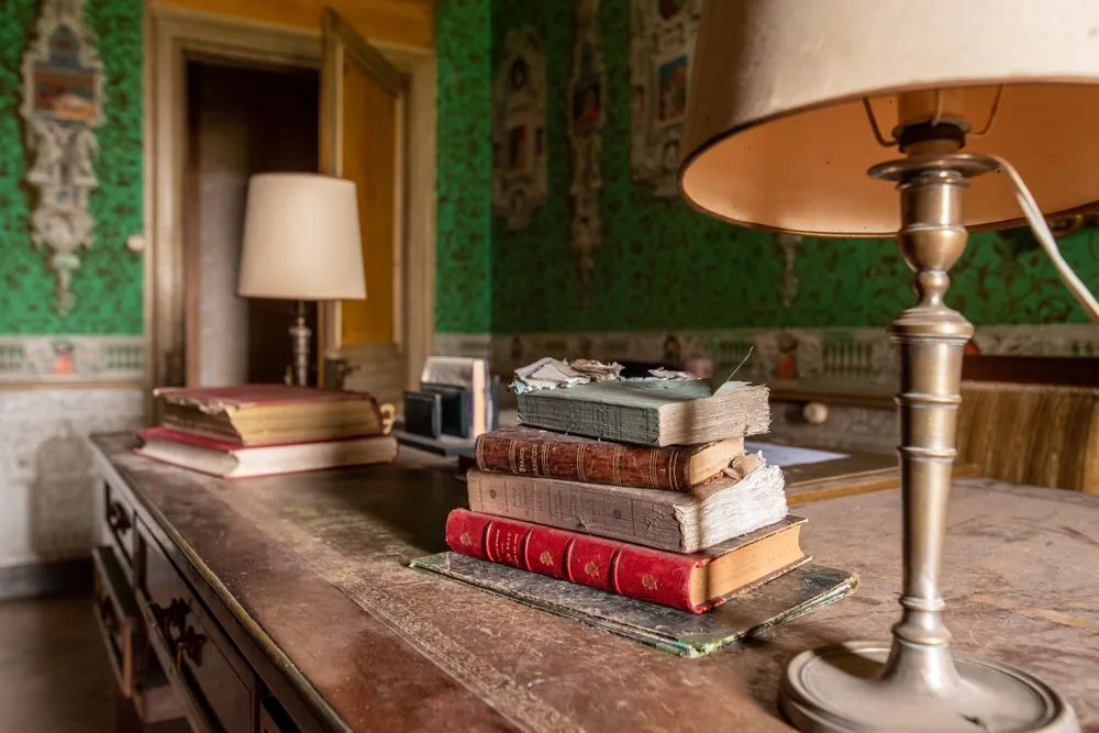 Antique book stack on a dusty writing desk inside an ornate abandoned chateau study
